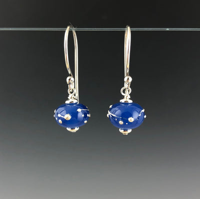 Luna Constellation Earrings by Becky Congdon are handmade glass beads in an opaque rich blue with raised strings and dots of fine silver wrapped around the bead. Each bead dangles from Bali silver simple ear wire with sterling silver small saucer beads on the top and bottom of the bead.