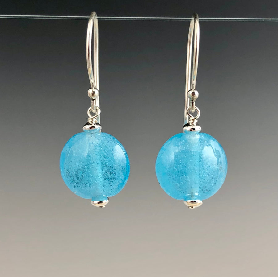 Aquamarine handmade glass beads with tiny air bubbles. Each bead is lentil in shape and dangles from sterling silver Bali ear wires with small silver saucer beads on either side of the glass bead. 