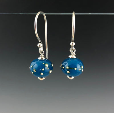 Atlantis Constellation Earrings by Becky Congdon are handmade glass beads in an opaque turquoise blue with raised strings and dots of fine silver wrapped around the bead. Each bead dangles from Bali silver simple ear wire with sterling silver small saucer beads on the top and bottom of the bead.