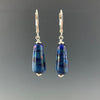 Tapered cobalt blue with shimmering light blue lines wrapped around beads dangle from silver leverbacks with small silver saucer beads on top and bottom of the earrings.