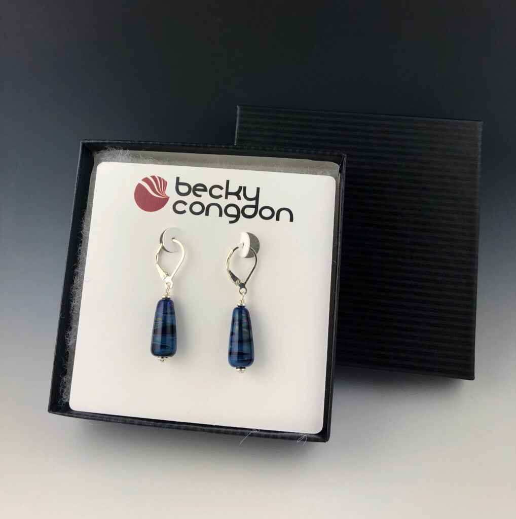 The cobalt blue dangle earrings are mounted on an earring card inside a black pin stripe gift box.
