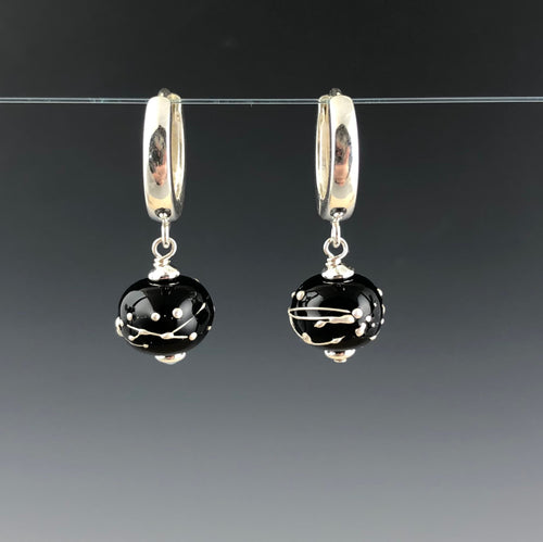 Black Constellation Hoop Earrings by Becky Congdon are handmade black glass beads with fine silver lines and dots wrapped around the beads. Each earring has a modern hinged hoop which has the bead dangling with silver saucer beads on the top and bottom of the glass bead.