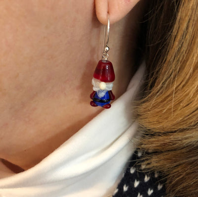 Gnome or Nisser glass bead earrings with red hats, blue outfit, red boots, white hair, beard, and mustache with round nose. The beads are on simple sterling silver ear wires. Shown on the wearer. Ready for a Scandinavian Christmas!