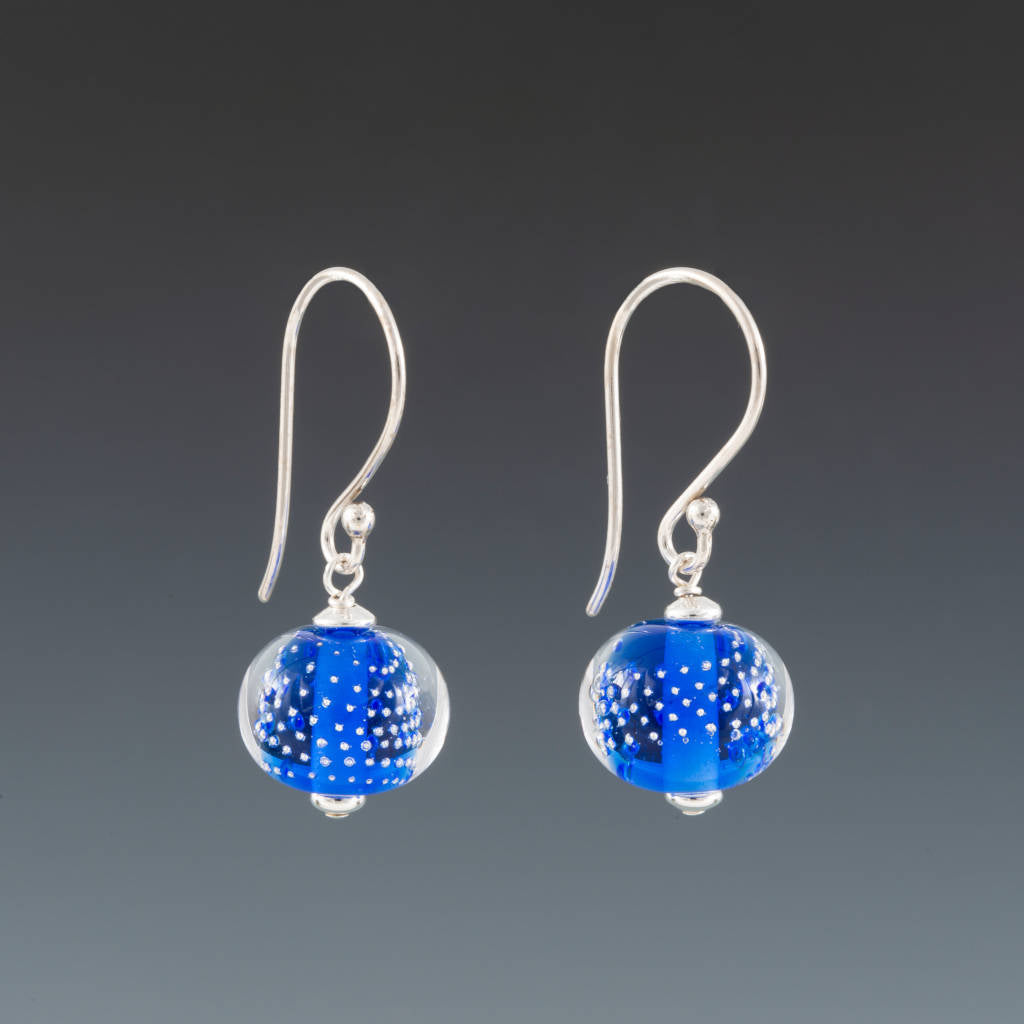 Intense Blue Sparkling Earrings (Ear Wires) by Becky Congdon are handmade glass beads of a bright intense blue with silver tiny balls encased in clear over the blue. The beads dangle from Bali silver ear wires with small silver saucer bead on either side of the bead.
