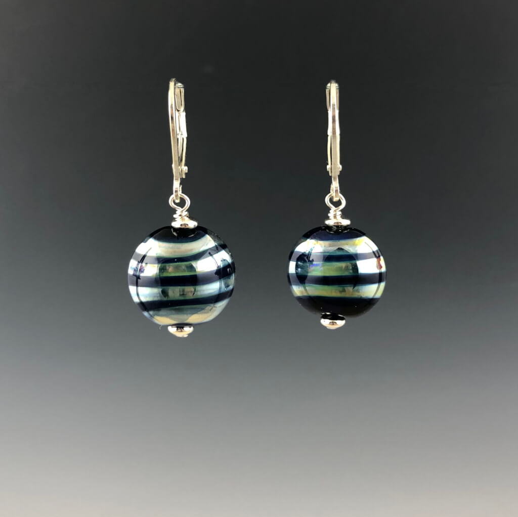 Handmade cobalt blue lentil-shaped beads with mirrored horizontal stripes dangle from silver leverbacks with small silver saucer beads on top and bottom of the glass beads.