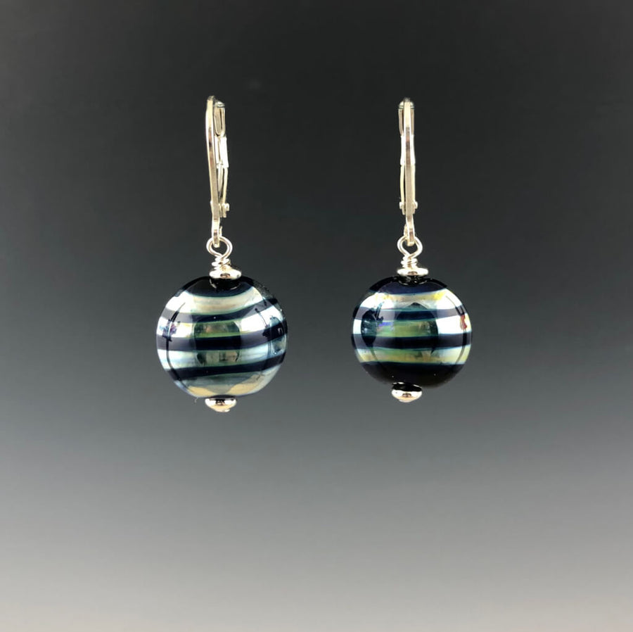 Handmade cobalt blue lentil-shaped beads with mirrored horizontal stripes dangle from silver leverbacks with small silver saucer beads on top and bottom of the glass beads.